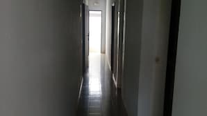 A long, narrow hallway with a tiled floor and white walls. There are doors on both sides of the hallway, and a bright light at the end. - Auberge Du Municipal (Bouake)