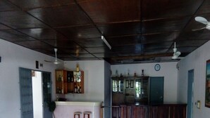 A spacious room with a high ceiling, a bar area with stools, a dining table with chairs, and a clock on the wall. - Auberge Du Municipal (Bouake)