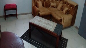A living room with a brown sofa, a small wooden table, and a red bench. - Auberge Du Municipal (Bouake)