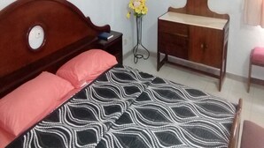 A bedroom with a wooden bed, a bedside table, a dresser, and a mirror. - Auberge Du Municipal (Bouake)