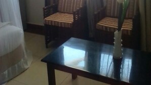 A room with two striped armchairs, a small table with a vase of flowers, and a window with curtains. - Dlux Hotel (Nakuru)