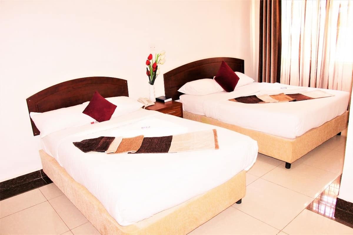 Two single beds with wooden headboards, white bedding, and a small bedside table with a vase of flowers.