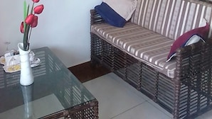 A living room with a sofa, a glass coffee table with a vase of flowers, and a flat-screen TV mounted on the wall. - Dlux Hotel (Nakuru)