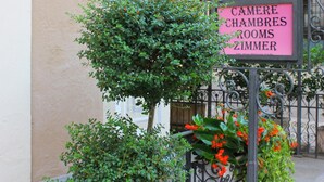 Naamplaatje met 'CAMERE CHAMBRES ROOMS ZIMMER', met een kleine boom en bloemen ervoor.