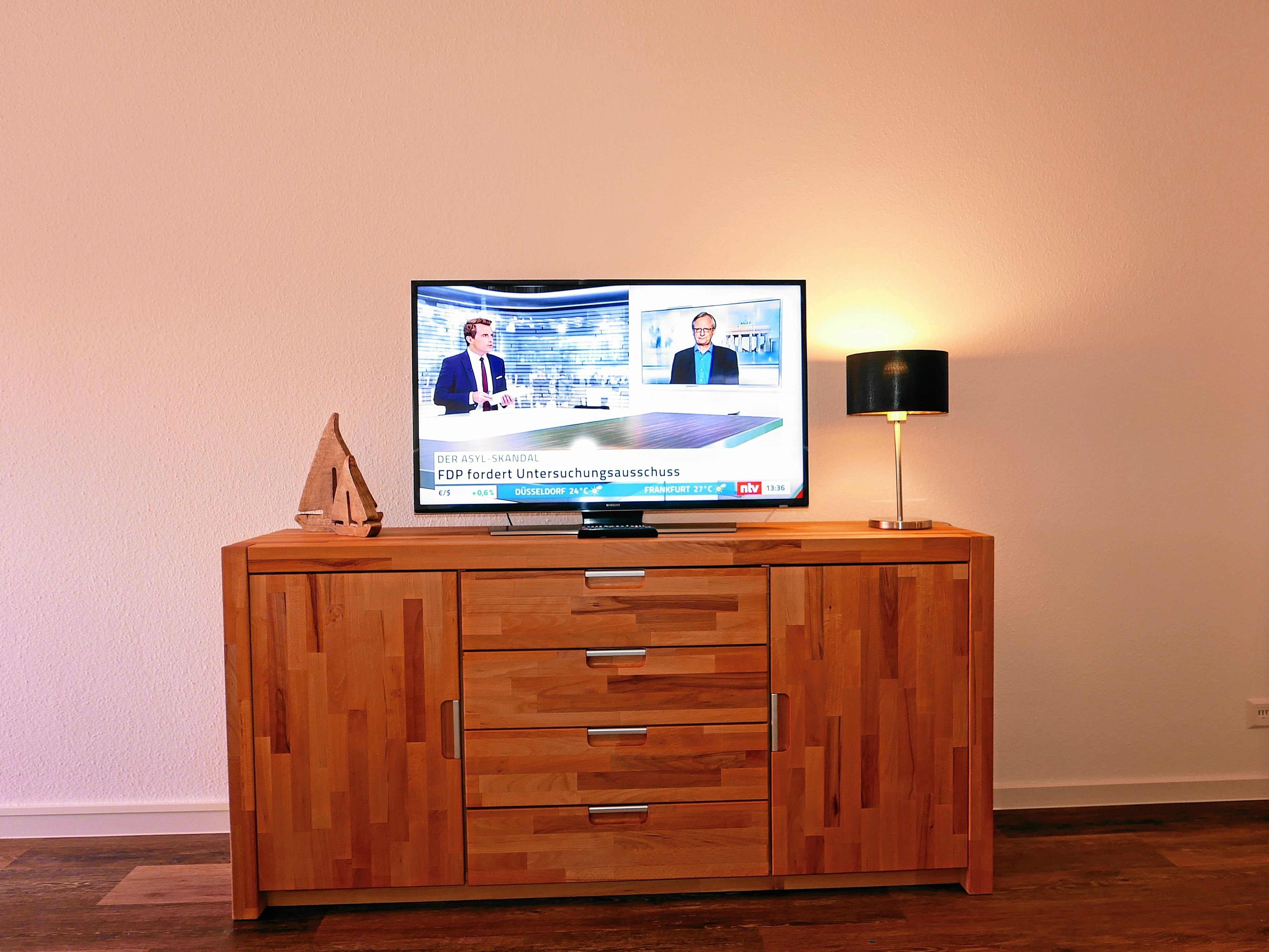 Ein Fernseher auf einer Holzkombination mit Schubladen, eine Lampe und eine Wand mit strukturierter Oberfläche.