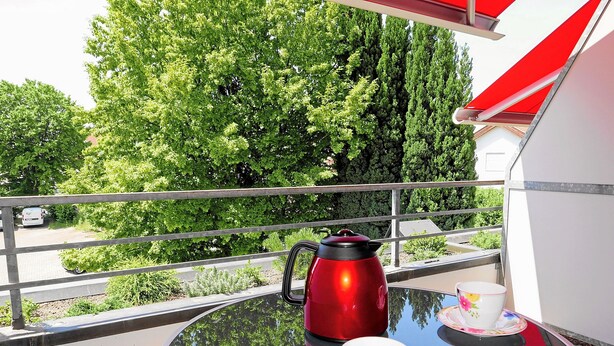 A balcony with a table set for tea, a red kettle, and a floral cup and saucer. - Ferienapartment Boot (Meersburg)