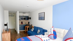 A modern hotel room with a blue and white patterned bed, a white sofa, a small dining table, and a kitchenette in the background. - Ferienapartment Boot (Meersburg)