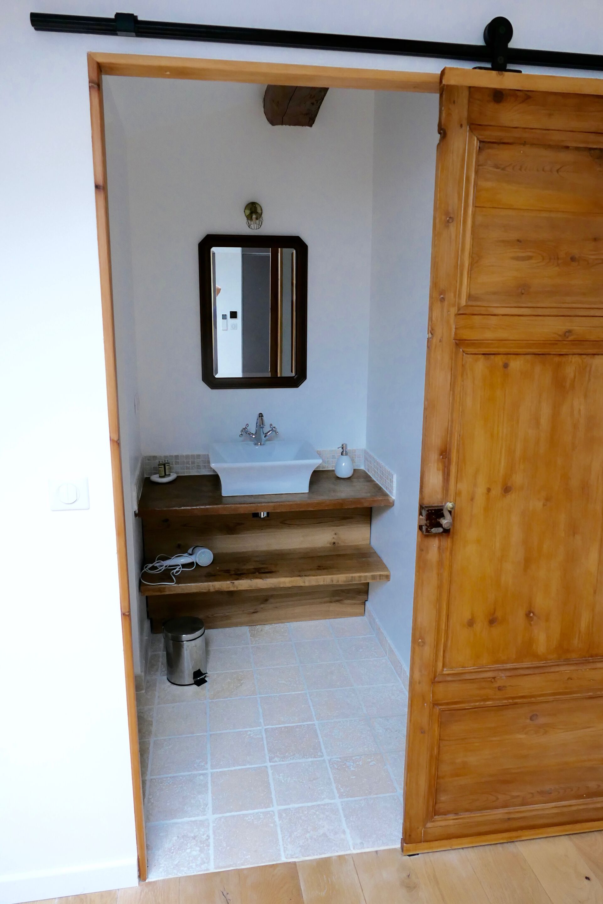 Een badkamer met een houten deur, een wastafel, een spiegel en een prullenbak.