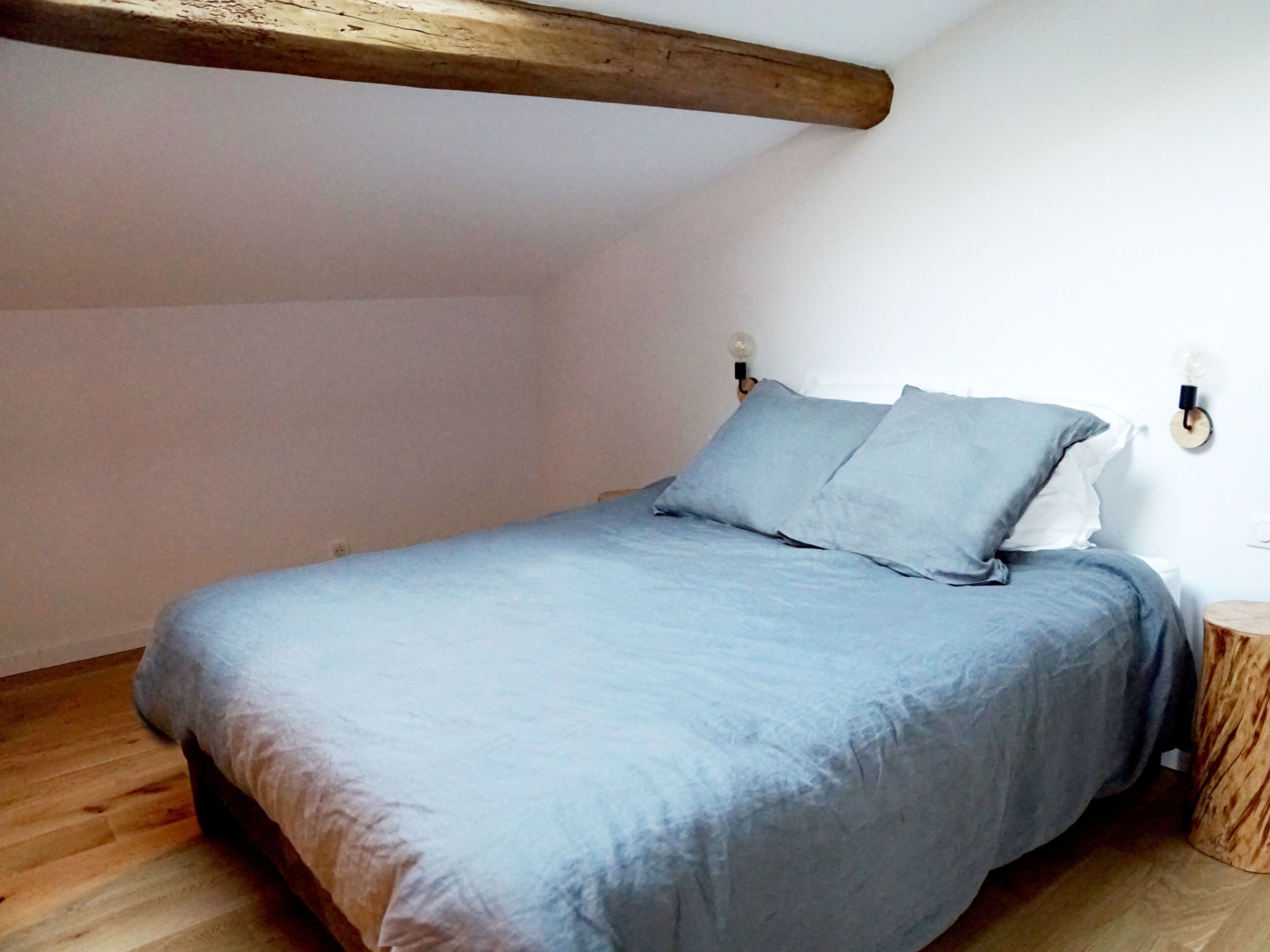 Ein Schlafzimmer mit Bett, Holzbalken, einem Nachttisch und Wandleuchten.