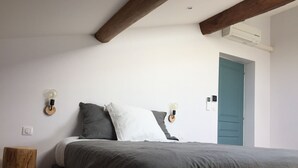 A bedroom with a bed, two wall-mounted light fixtures, a wooden nightstand, and a door. - La Garoffe (Pibrac)
