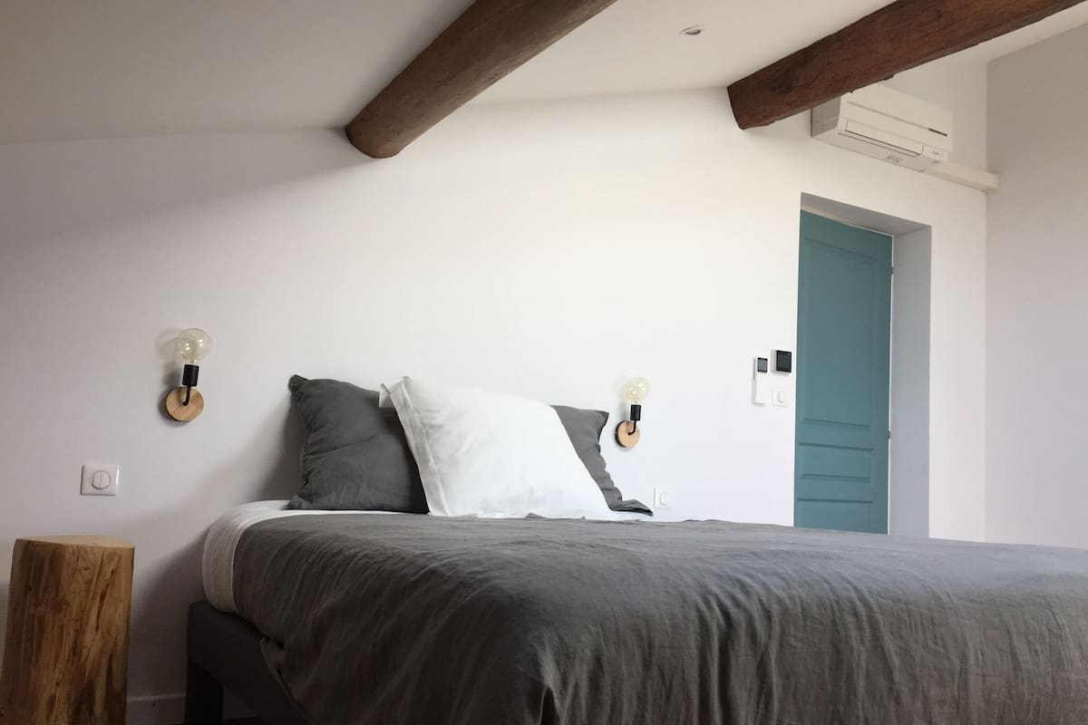 A bedroom with a bed, two wall-mounted light fixtures, a wooden nightstand, and a door.