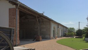 A building with a covered outdoor area, a gravel driveway, and a well-maintained lawn. - La Garoffe (Pibrac)