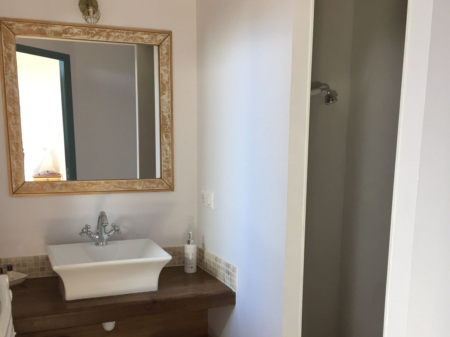 A bathroom with a white sink, a mirror with a decorative frame, and a shower.