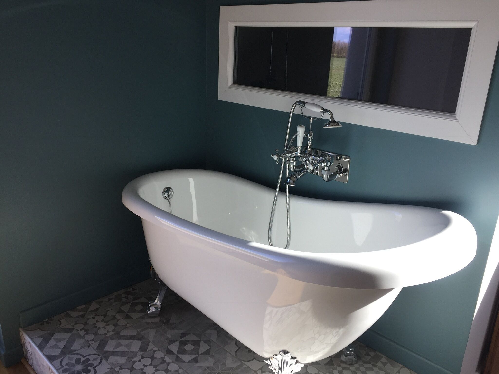 Une baignoire sur pieds dans une salle de bain dotée d’un carrelage géométrique et de murs de couleur turquoise.