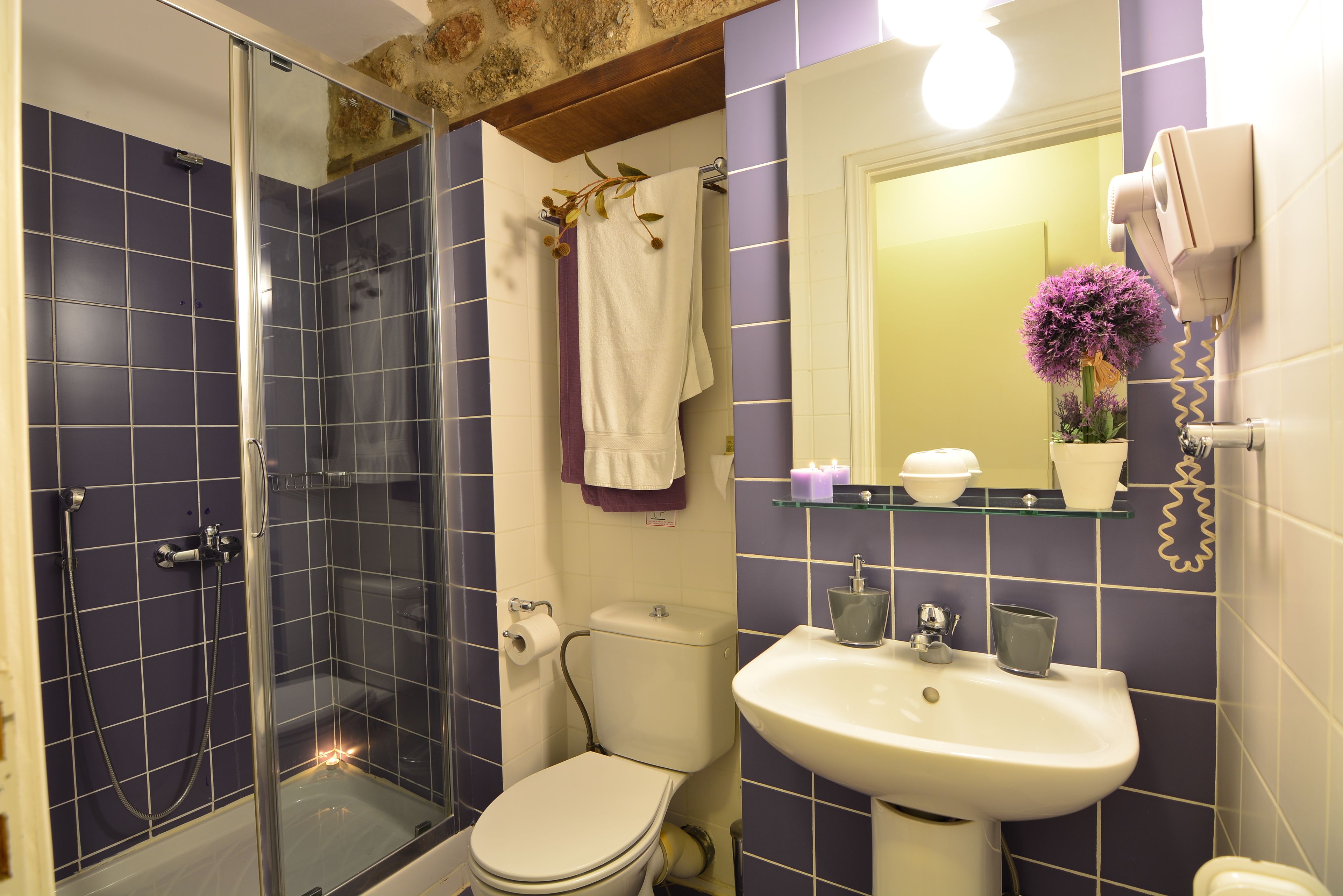 Un baño con ducha de mampara de vidrio, inodoro blanco, lavamanos y espejo con un florero.