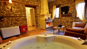 Une pièce aux murs de pierre, dotée d’une grande baignoire, d  ’une cheminée et d’un coin salon confortable.