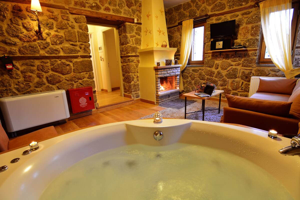 Une pièce aux murs de pierre, dotée d’une grande baignoire, d’une cheminée et d’un coin salon confortable.