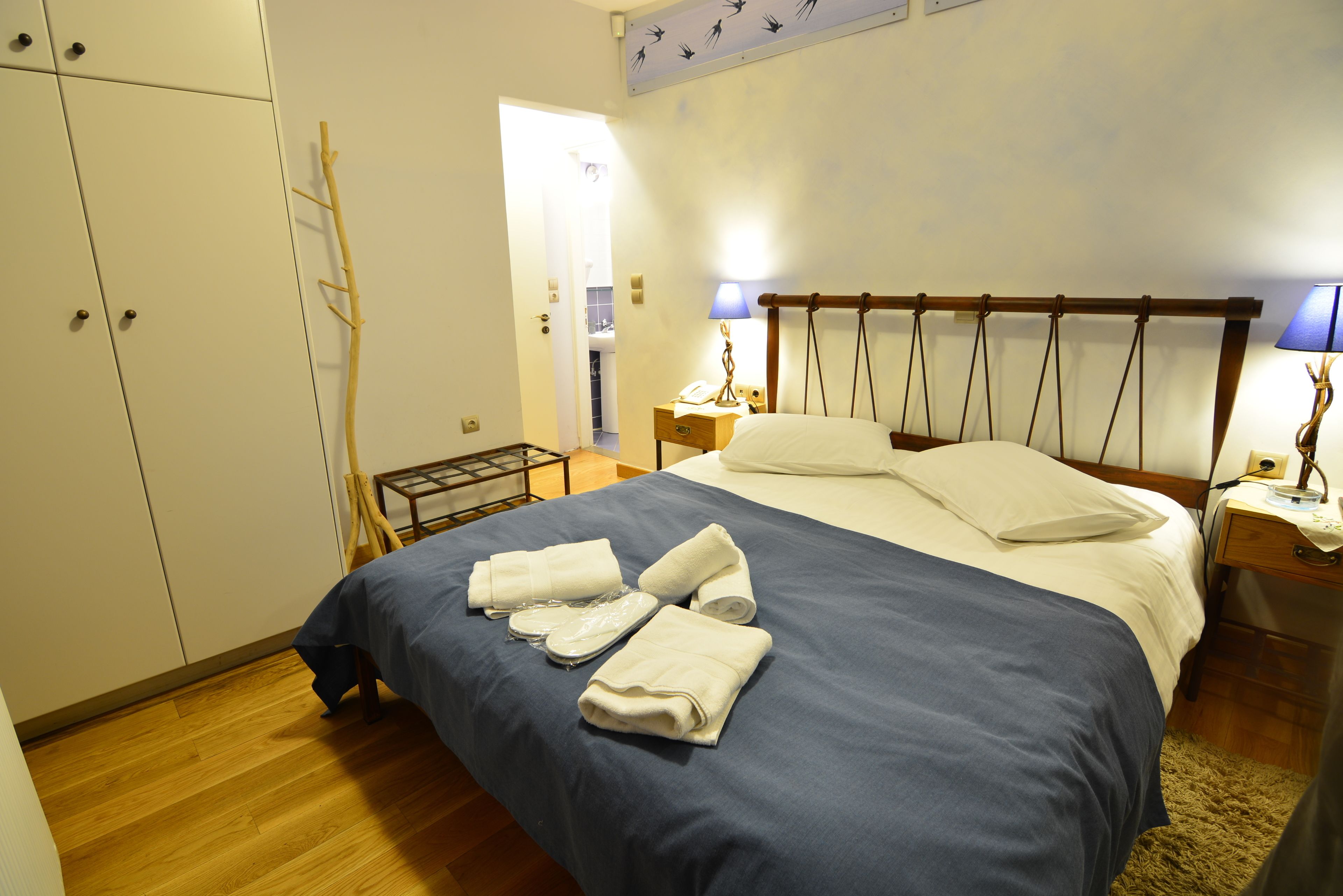 A neatly made bed with a blue bedspread and white pillows, a wooden nightstand with a lamp, and a wardrobe with a mirror.