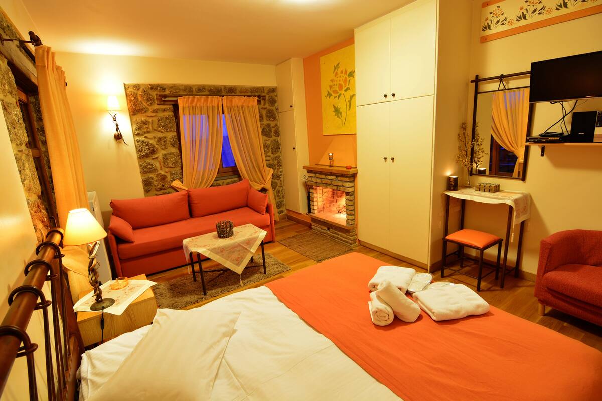 Une chambre d’hôtel comprenant un lit, un canapé, une petite table, une chaise, une cheminée et un téléviseur.