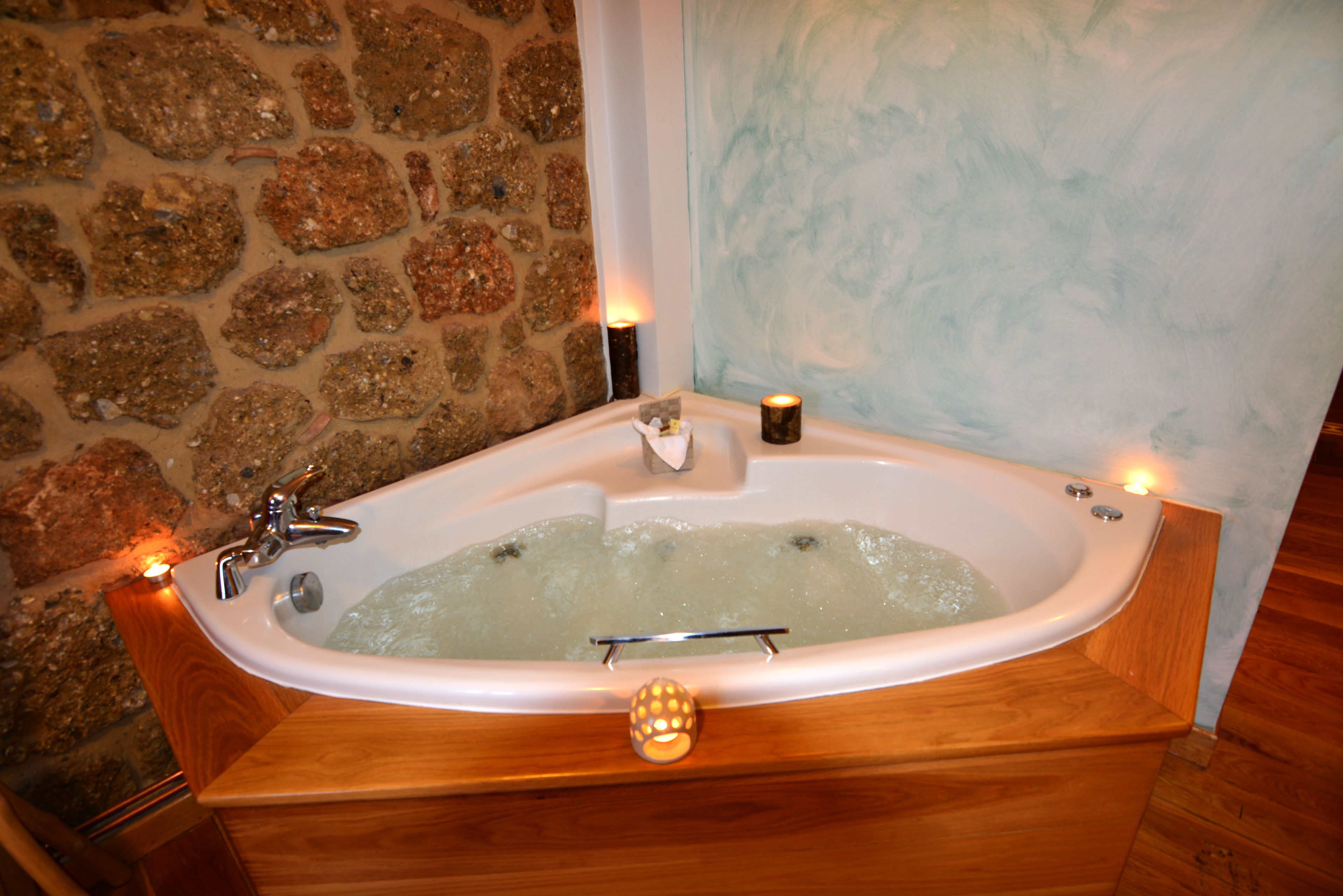 A stone wall, a bathtub with candles, and a wooden bench.