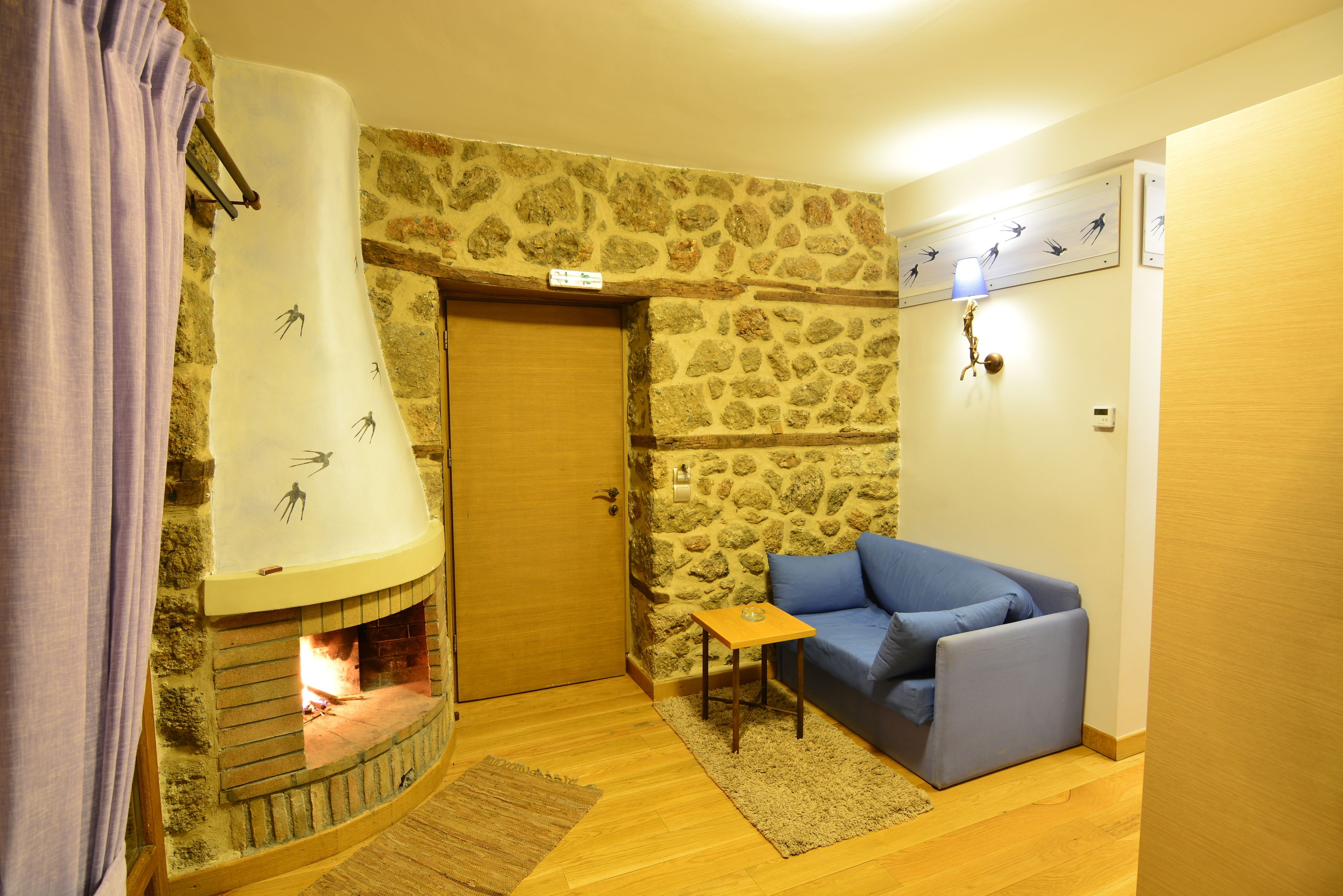 Una habitación acogedora con pared de piedra, chimenea, sofá azul y una mesita.