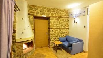 Una habitación acogedora con pared de piedra, chimenea, sofá azul y una mesita.