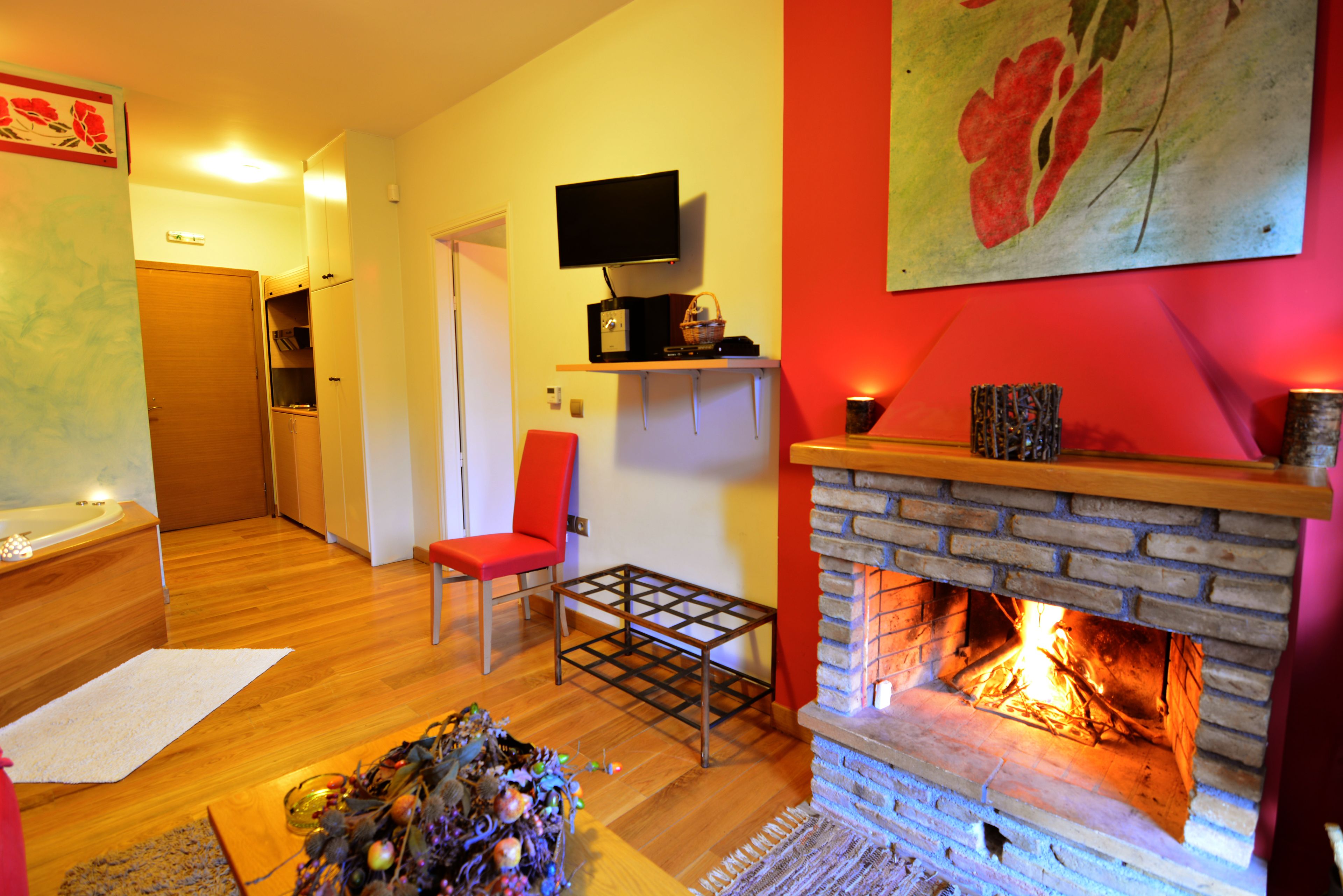 Una sala de estar con chimenea, un televisor en un estante y un sillón rojo.