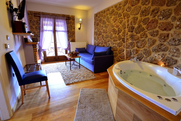 A room with a stone wall, a blue sofa, a wooden chair, a small table, and a bathtub.