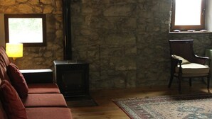 Een knus interieur met een stenen muur, een open haard, een bank, een stoel en een vloerkleed.