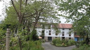 Een gebouw met twee verdiepingen en een pannendak, omringd door weelderige begroeiing en een grindpad.