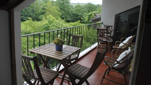 Een balkon met houten meubels, een bloempot en uitzicht op weelderige begroeiing.