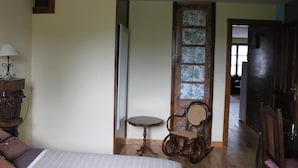Een kamer met een bed, een klein rond tafeltje, een rieten stoel en een deur naar een andere kamer.