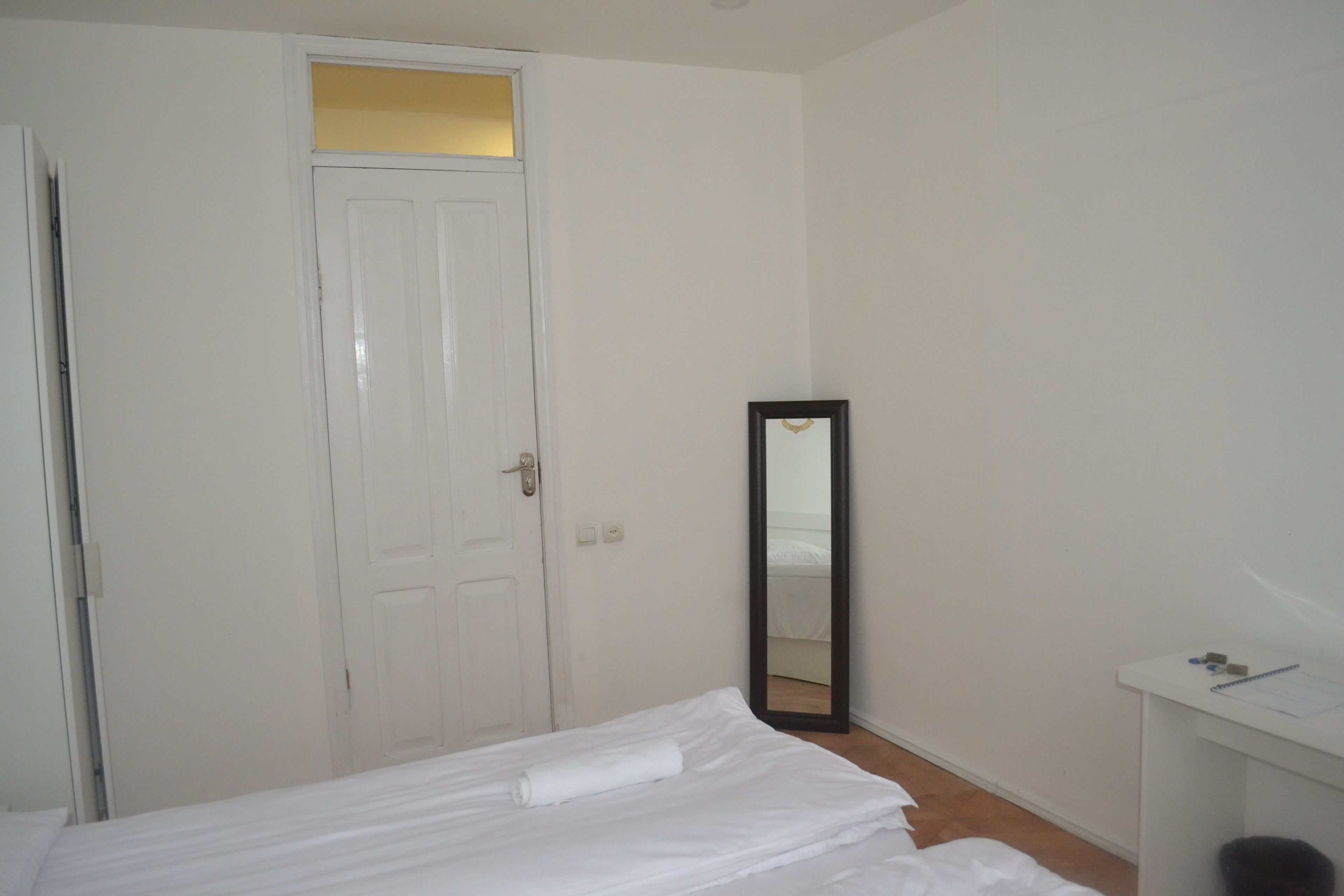 A bedroom with a bed, a white wardrobe, a mirror, and a small desk with a chair.