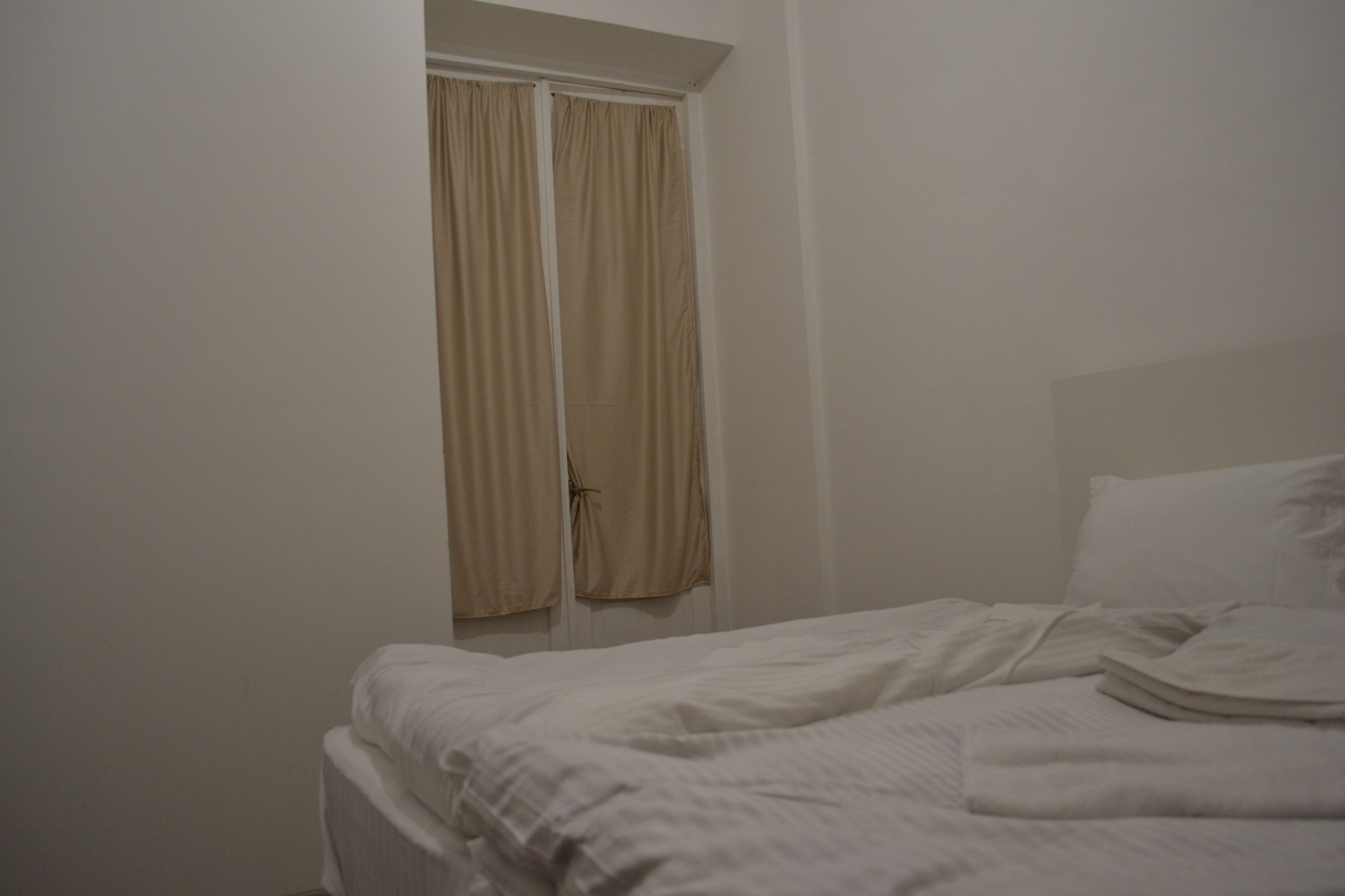 A bedroom with a bed, a door, and a window with curtains.