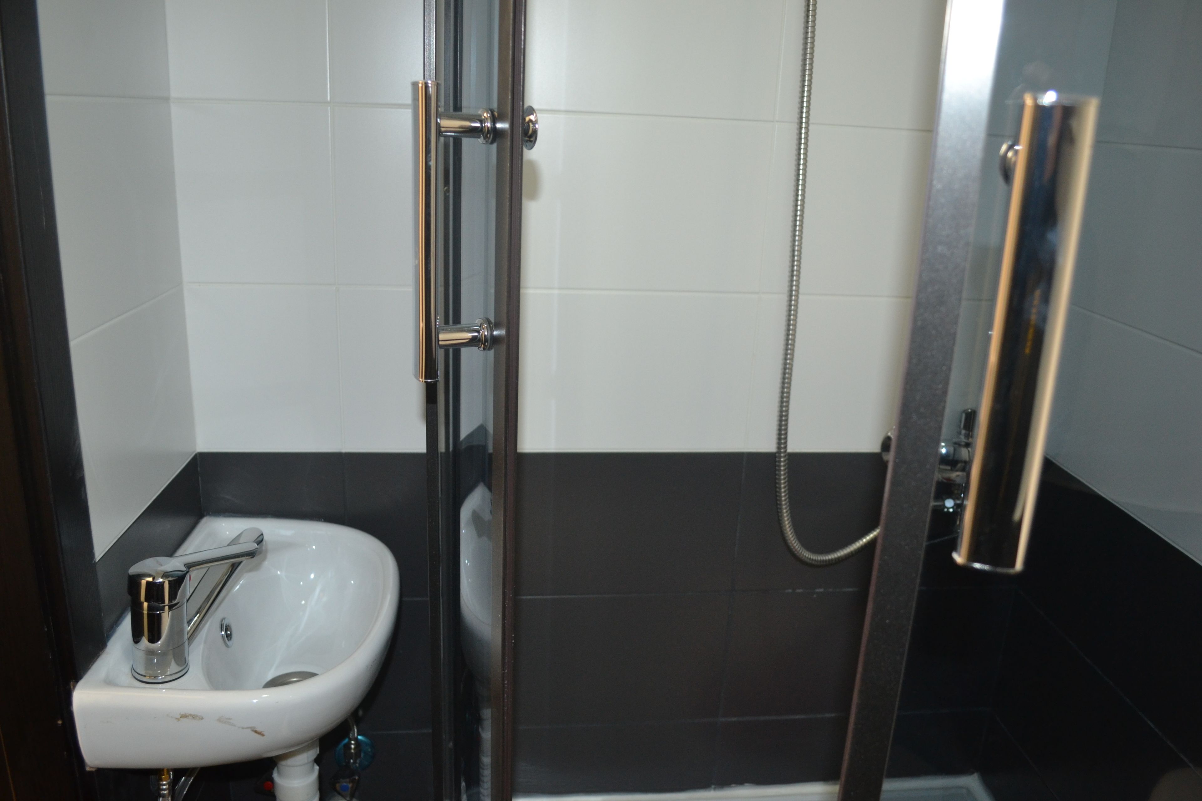 A bathroom with a white sink, a glass shower enclosure, and black tiled walls.