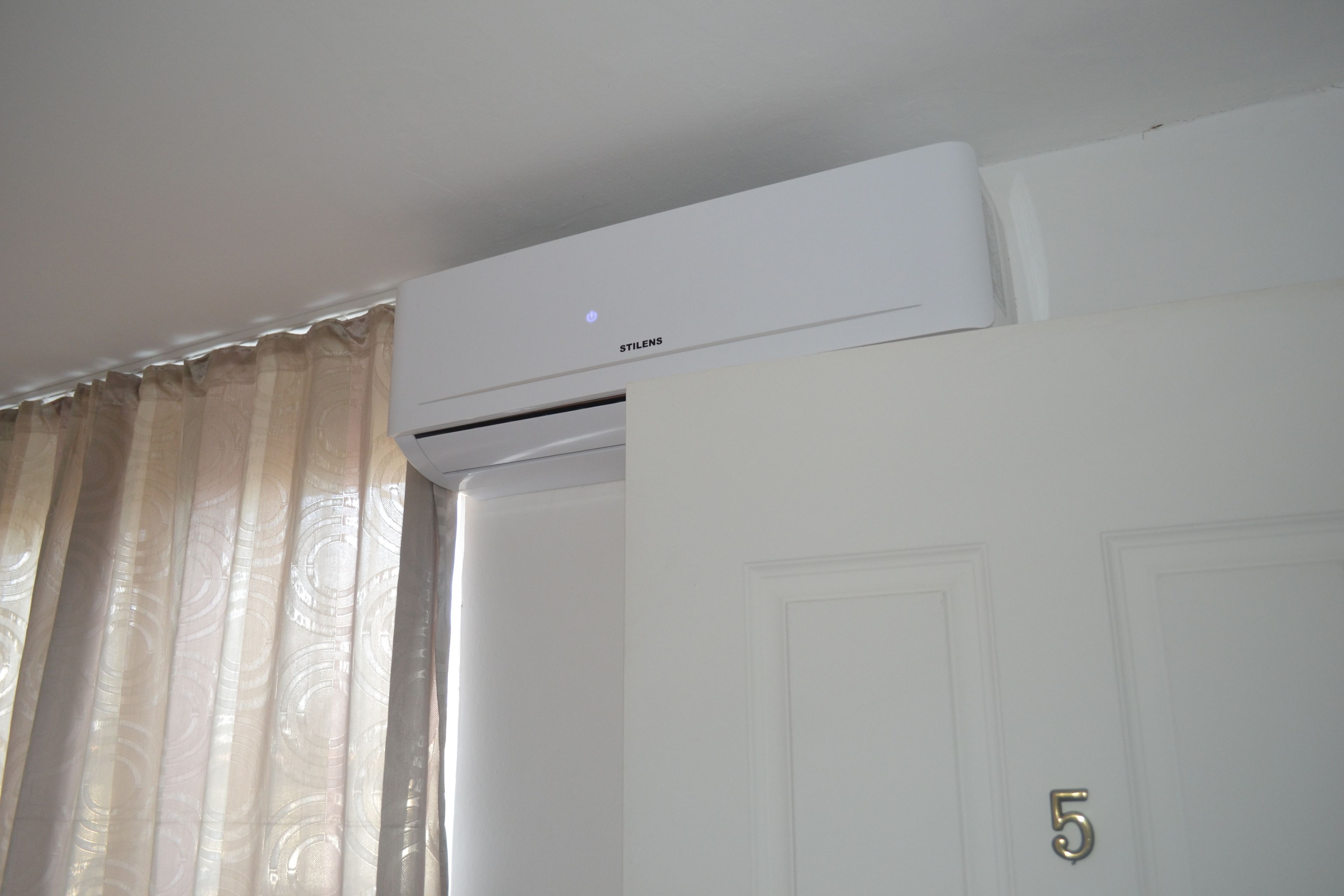A white air conditioning unit mounted on a wall above a closed door with a number '5' on it.