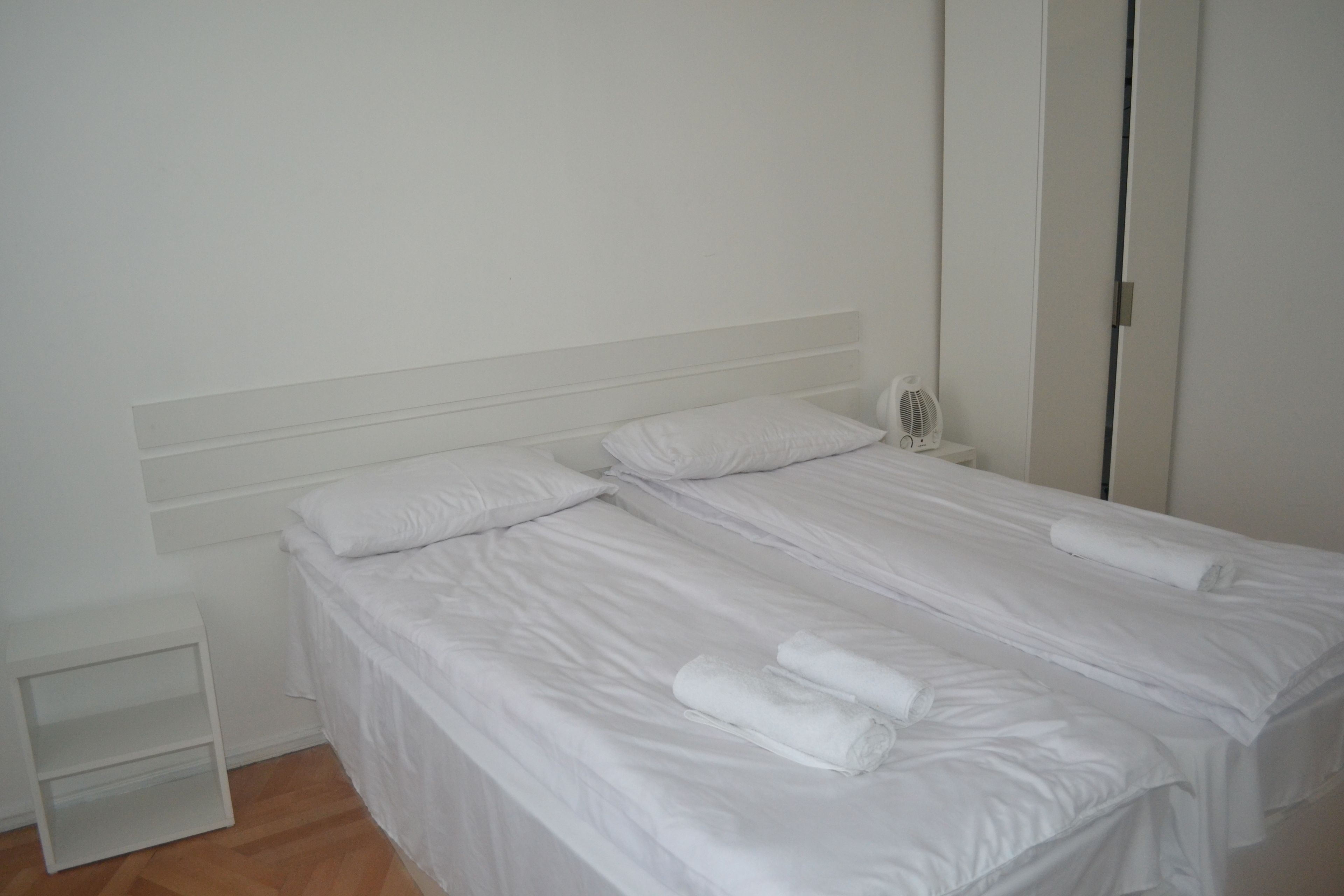 Een keurig opgemaakt bed met witte lakens en twee opgerolde handdoeken.