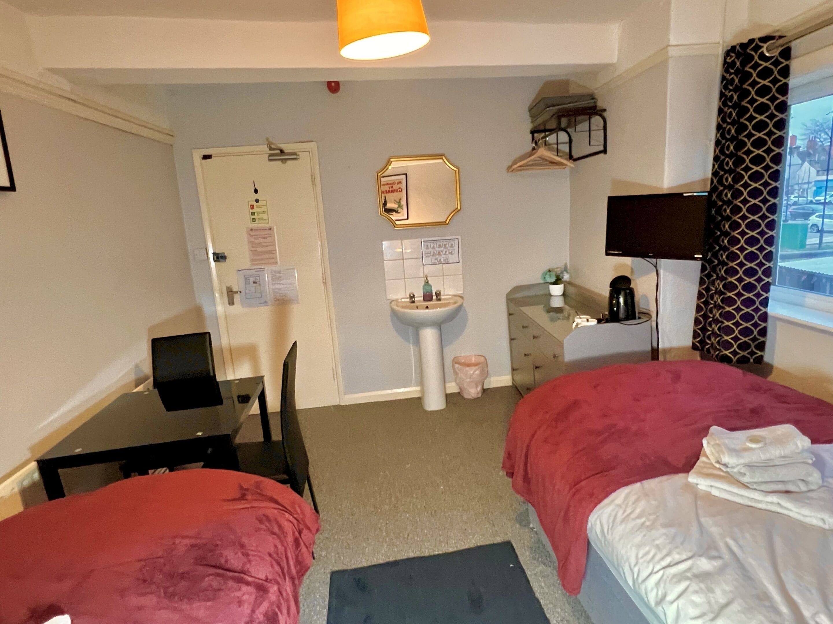 A hotel room with two beds, a desk, a chair, a sink, a mirror, a television, and a window with a view.