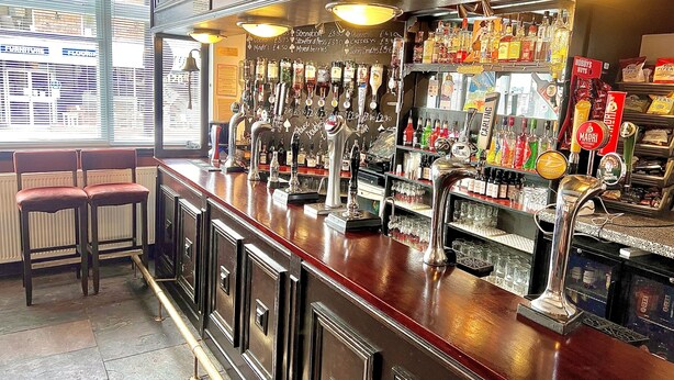 Un bar doté de plusieurs robinets, d’étagères remplies de bouteilles d’alcool et d’un tableau affichant le menu.
