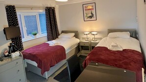 Une chambre d’hôtel avec deux lits, une fenêtre avec des rideaux, une affiche encadrée au mur et un bureau avec une lampe.