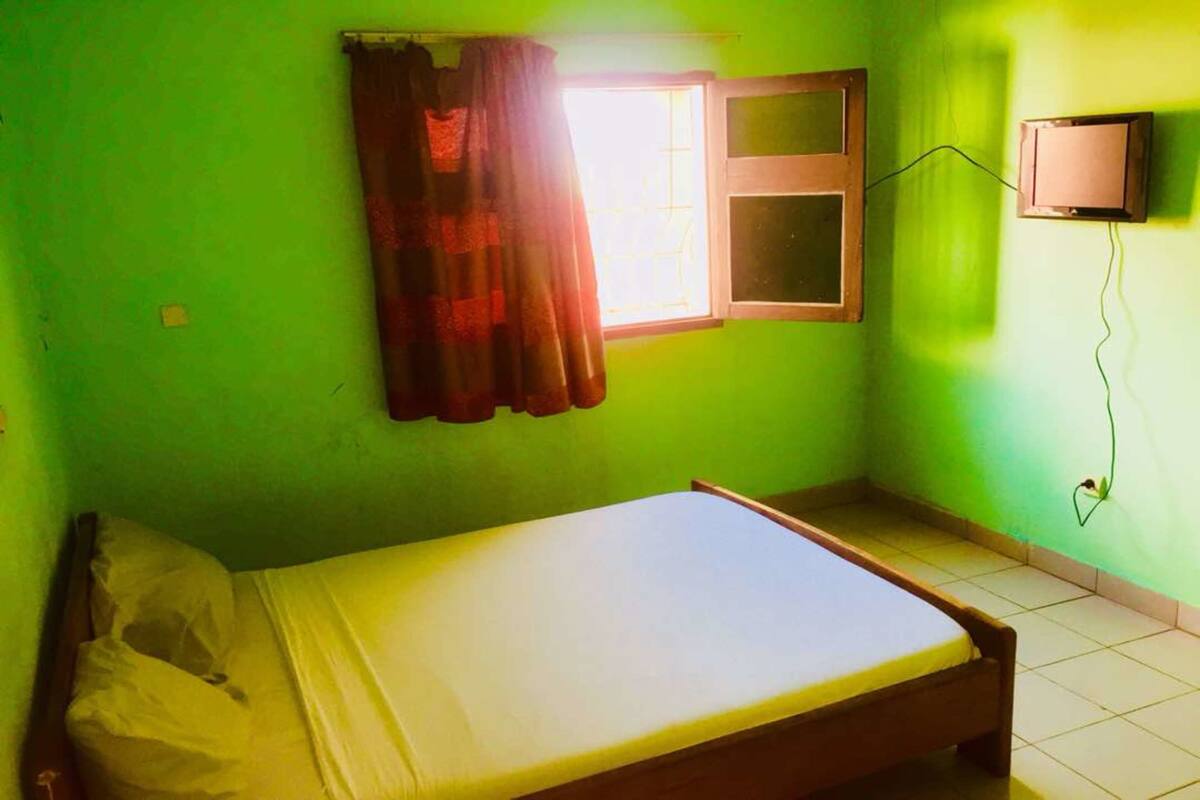 A small, single-bed room with a window, a wall-mounted television, and a power outlet.