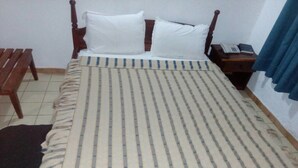 Una cama individual con una colcha a rayas, una mesita de noche de madera con un teléfono y un banco a la izquierda.
