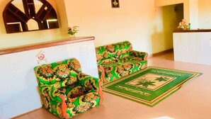 Una zona de recepción con dos sofás tapizados en verde, una pieza decorativa en la pared y una alfombra verde con un diseño de hojas.