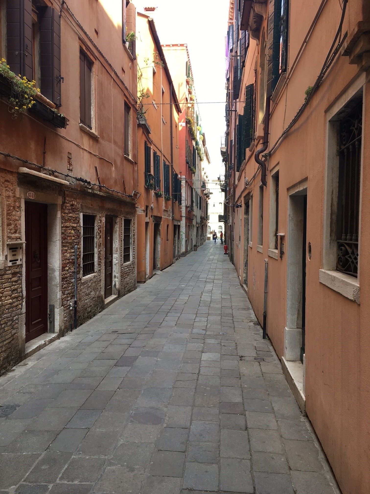 A narrow cobblestone street flanked by historic buildings with shuttered windows and balconies.