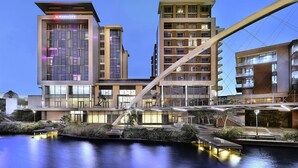 A modern hotel with a prominent 'Marriott' sign, a waterfront location, and a pedestrian bridge connecting different parts of the property. - Island Letting-Crystal towers (Cape Town)