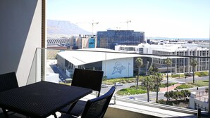 A balcony with a table and chairs, overlooking a cityscape with modern buildings and a clear sky. - Island Letting-Crystal towers (Cape Town)