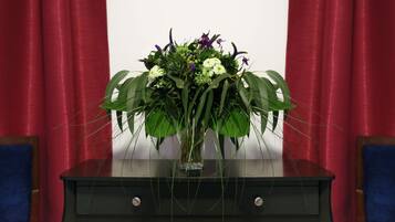 A bouquet of flowers in a vase on a black table with two drawers, set against a red curtain backdrop.