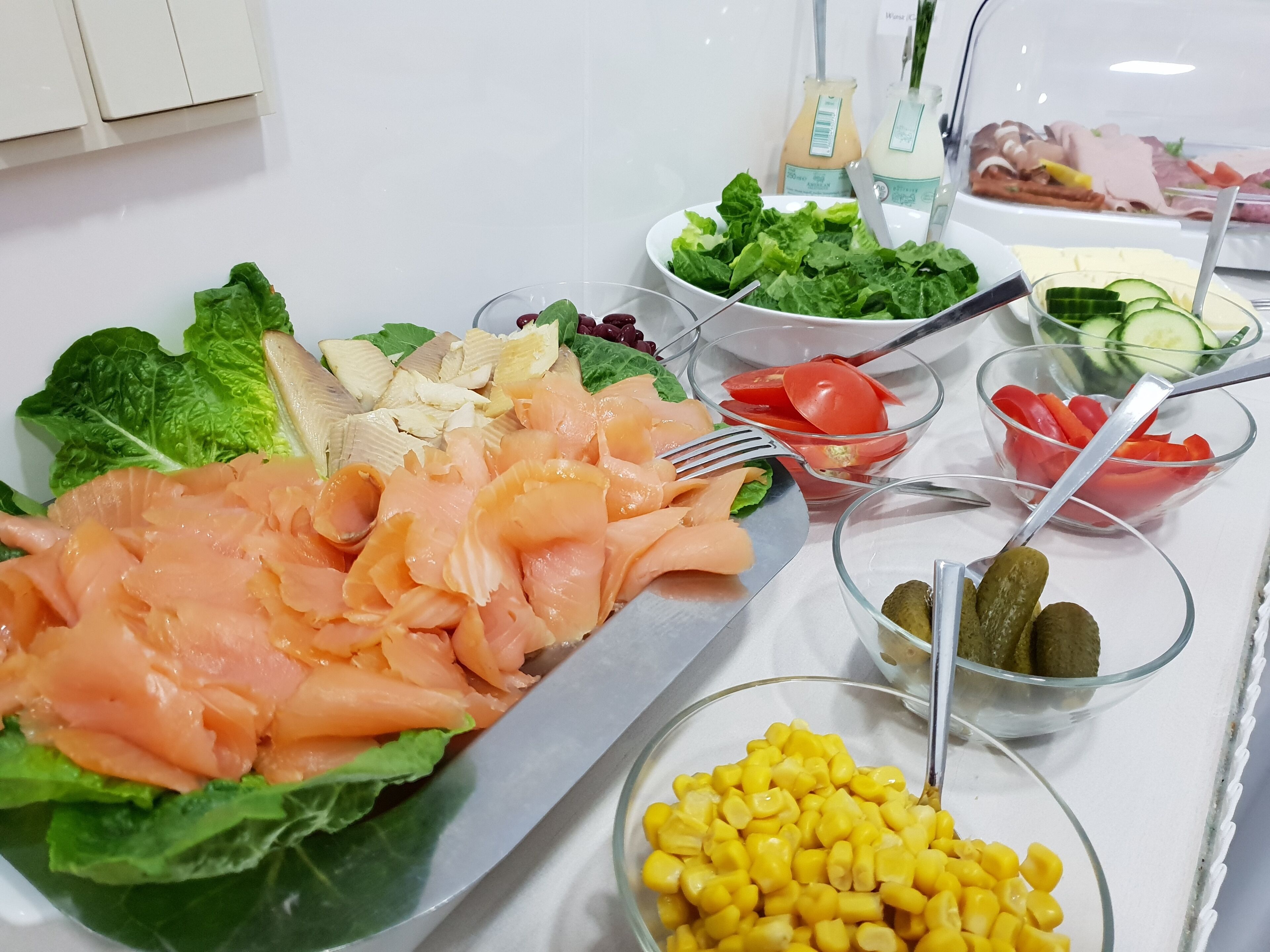 Un buffet proposant une variété de plats, notamment du saumon, de la laitue, des tomates, des concombres et du maïs.