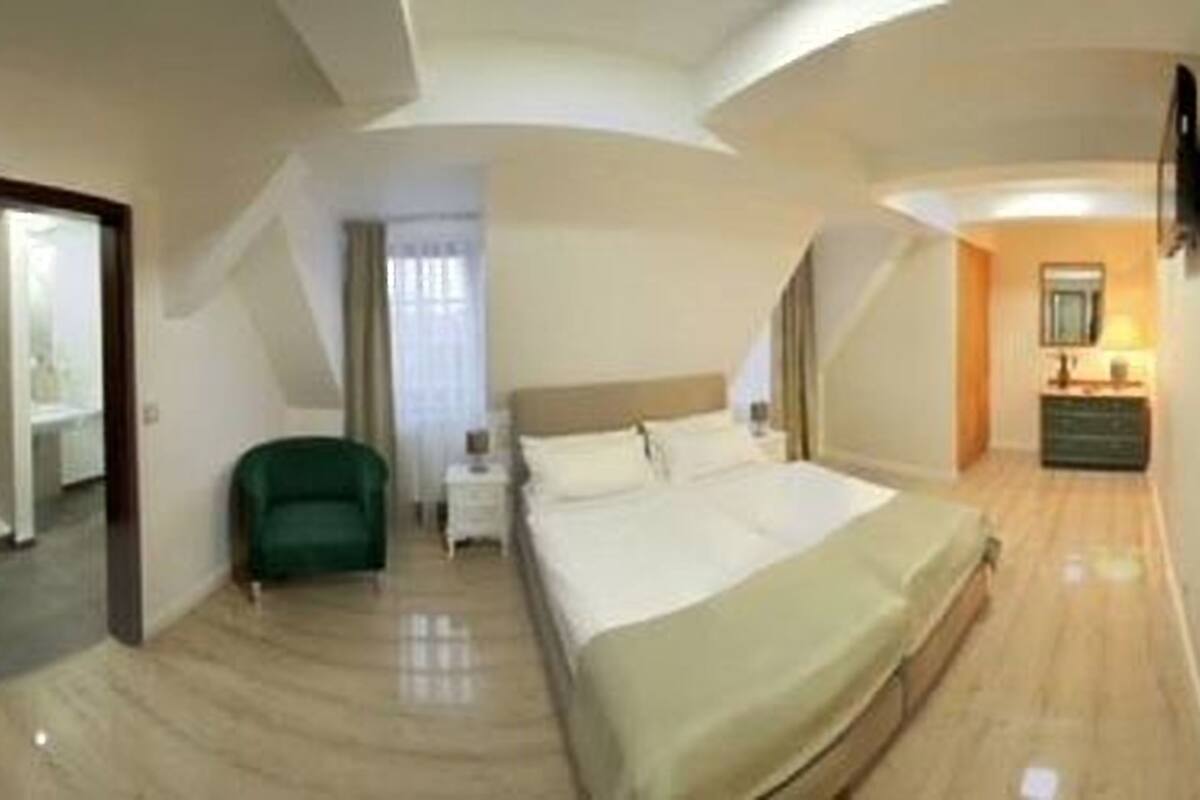 A hotel room with a bed, a green armchair, a nightstand, and a dresser.