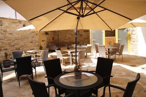An outdoor patio area with stone walls, wicker furniture, and a large umbrella providing shade. - Micha'S Hotelbetriebe – Hotel Am Markt (Oebisfelde)